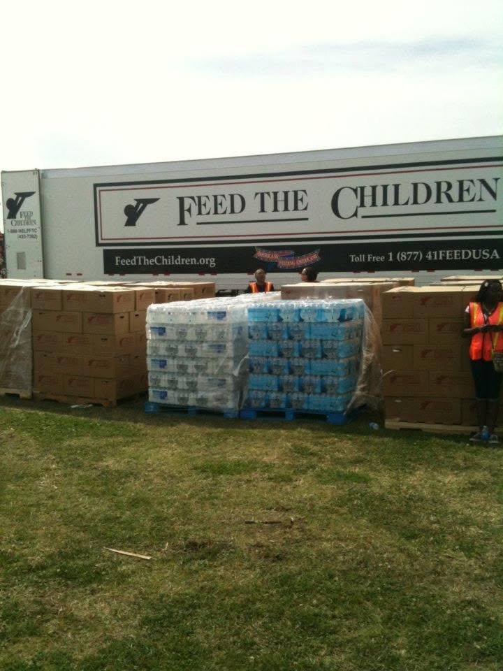 Feed the Children truck, bottled water, boxes, and supplies prepared for community distribution.